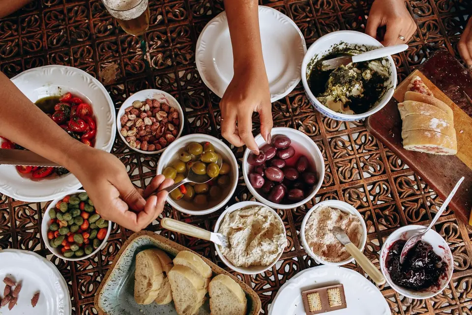 A Greek sharing table seen from above, with small plates, bread and hands reaching in, Greek catering, illustrative photo